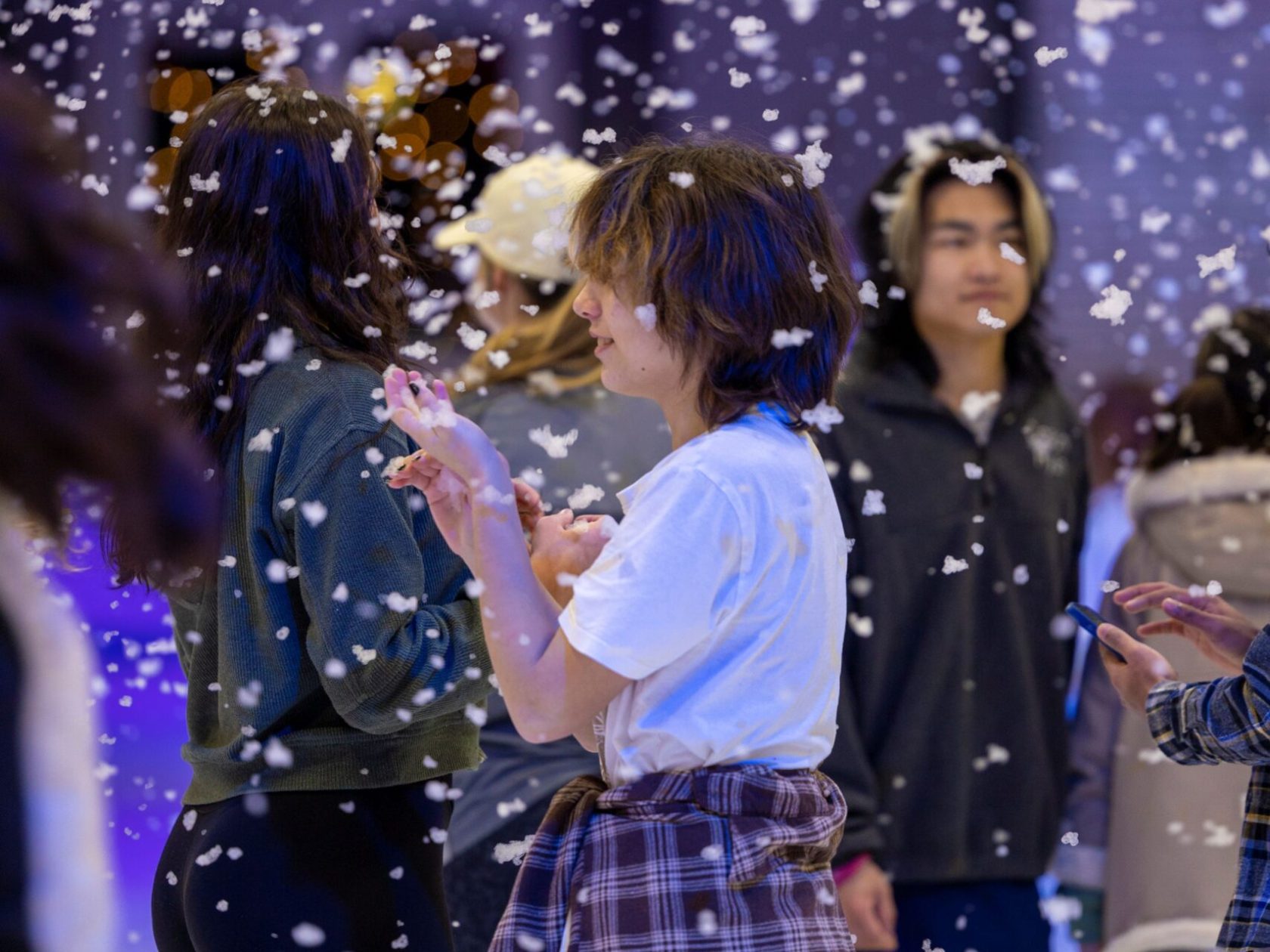 Artificial snow falls around skaters during a festive ice rink event.